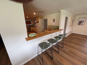 A modern kitchen with a wooden countertop, bar stools, and a view into the dining area. - The Lodge Farmhouse at Softfoot (Hindmarsh Valley)