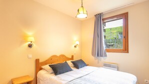 Ein Schlafzimmer mit einem Holzbett, zwei Nachttischlampen, einem Fenster mit Blick auf einen Garten und einem kleinen Nachttisch.