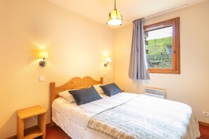 A bedroom with a wooden bed, two bedside lamps, a window with a view of a garden, and a small wooden nightstand. - Les Alpages du Corbier - A314 - Télésièges à 250 m (Villarembert)