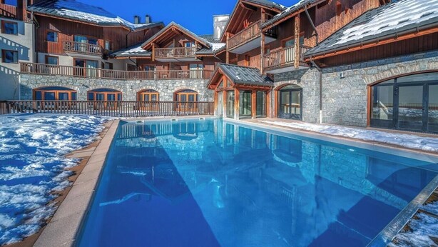 Ein Poolbereich mit einem Steinhaus, Holzbalkonen und blauem Himmel.