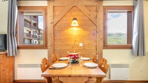 Ein Holzespeisetisch mit Stühlen, eine zentrale Tischlampe und Blick auf eine Berglandschaft durch ein Fenster.