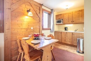 A wooden interior with a dining table set for four, a microwave, and a sink in the kitchen area. - Les Alpages du Corbier - A314 - Télésièges à 250 m (Villarembert)