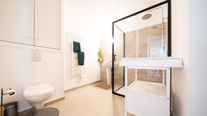 Moderni kylpyhuone, jossa on wc, pesuallas, suihku ja lasiseinällä erotettu suihkutila.