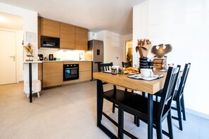 A modern kitchen with wooden cabinets, a microwave, and a dining area with a wooden table and black chairs. - Au pied du Prorel - Joli T3 à 150m télécabine (Briancon)