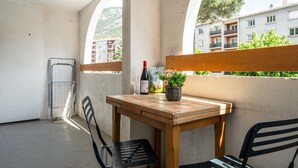Un balcón con mesa de madera, dos sillas, una botella de vino y un florero.