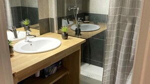 Un baño con tocador de madera, dos lavamanos, ducha con puerta de cristal y un espejo.