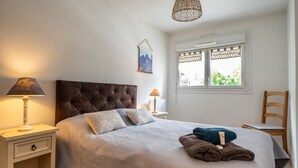 Un dormitorio con cabecera capitonada, una mesita de noche con lámpara, una ventana con vistas y una silla.