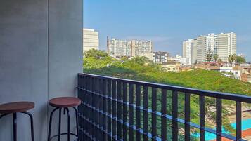 Ein Balkon mit zwei Hocker, einem Metallgeländer und Blick auf die Stadt.