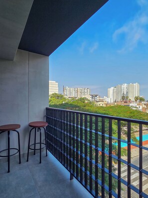 Ein Balkon mit zwei Hocker, einem Metallgeländer und Blick auf die Stadt.