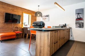A modern kitchen with a wooden island, a TV mounted on the wall, and a ski lift picture. - Chantloup - Appartement prestige à Chantemerle (Saint-Chaffrey)