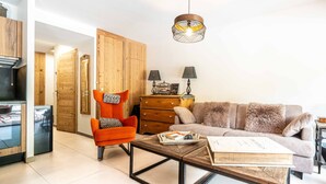 Ein Wohnzimmer mit Sofa, Sessel, Couchtisch, Holzschrank und einer Pendelleuchte.