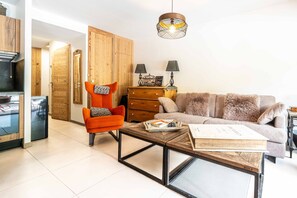 A living room with a sofa, armchair, coffee table, wooden cabinet, and a hanging light fixture. - Chantloup - Appartement prestige à Chantemerle (Saint-Chaffrey)