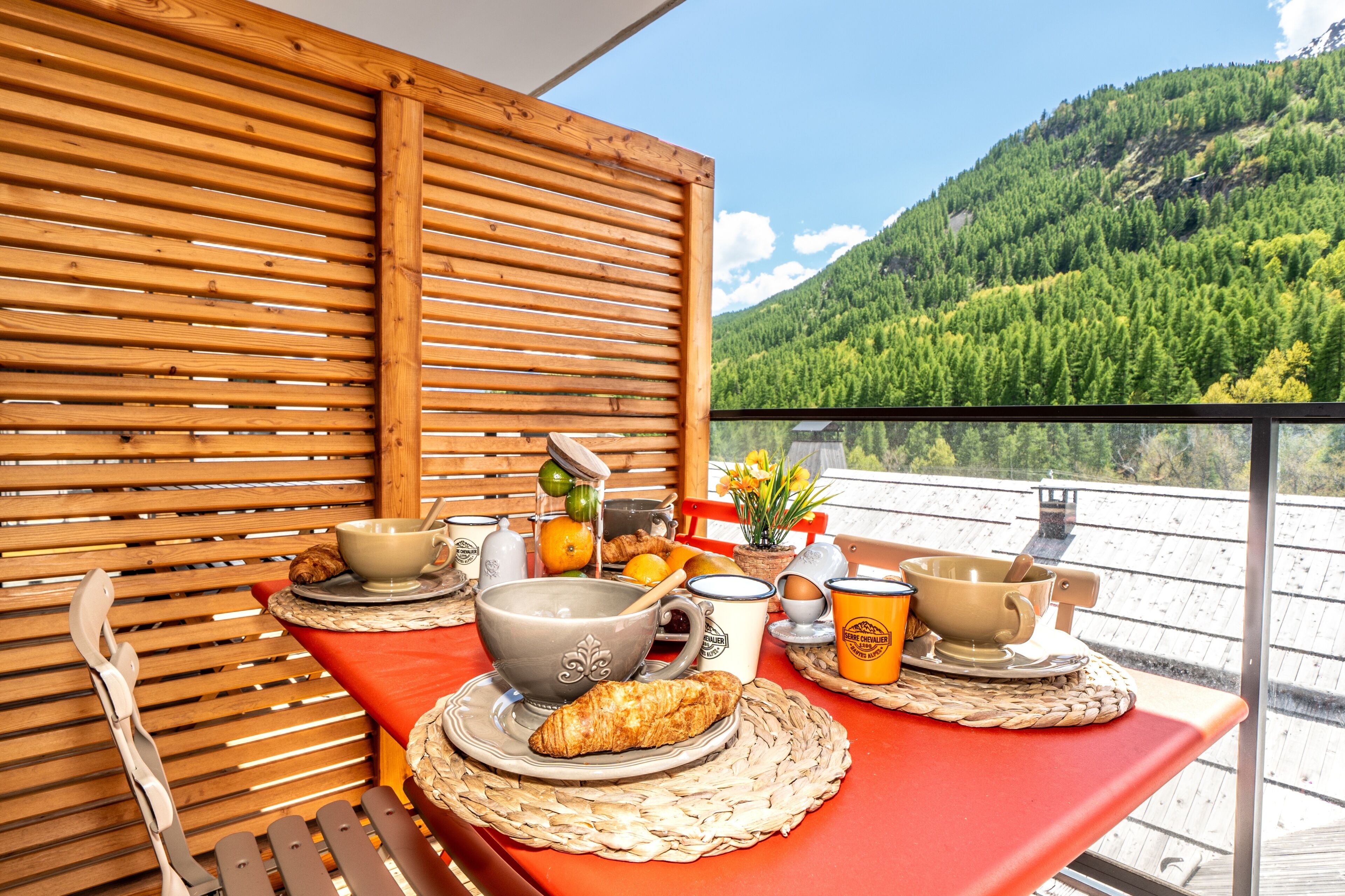 A table with breakfast items, a wooden slatted wall, and a mountain view.