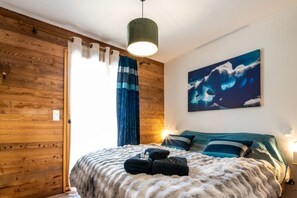 A room with wooden walls, a bed with a striped blanket, a painting of a wave, and a hanging light fixture. - Chantloup - Appartement prestige à Chantemerle (Saint-Chaffrey)