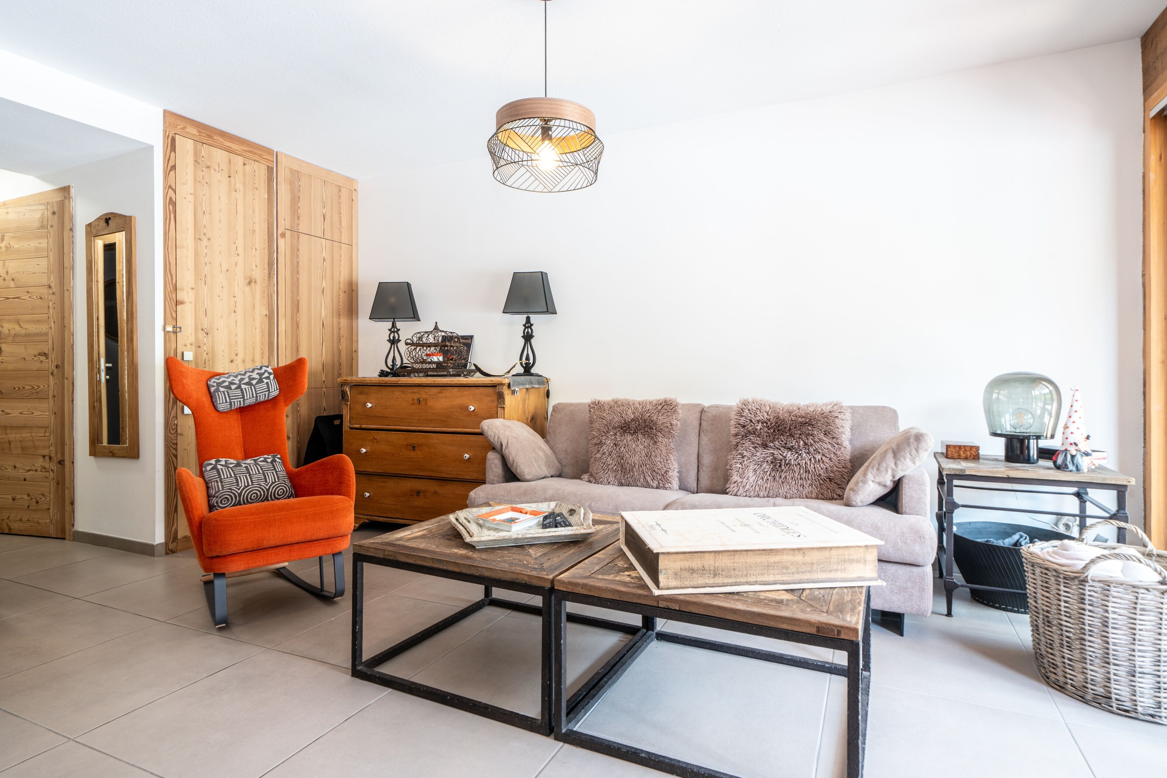 Un salon comprenant une armoire en bois, un fauteuil rouge, un canapé, une table basse et un luminaire suspendu.