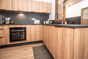 Eine moderne Küche mit Holzschränken, einem eingebauten Ofen und einer schwarzen Arbeitsplatte.