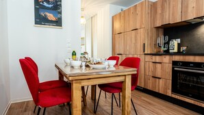 Una cuina moderna amb armaris de fusta, una taula de dinar amb cadires vermelles i un forn encastrat.