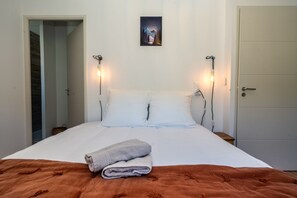 Ein Bett mit weißen Bettwäsche, zwei Nachttischlampen, ein gefaltetes Handtuch und ein Bild an der Wand.