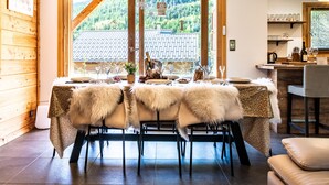 A dining area with a table set for four, a wooden interior, and a view of a mountain landscape through a large window. - Chalet Nanouk - exposé plein sud (La Salle-les-Alpes)