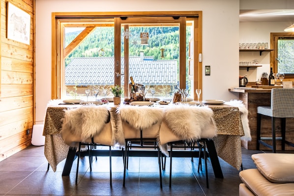 Un comedor con una mesa preparada para cuatro, interior de madera y vista a un paisaje montañoso a través de un ventanal grande.