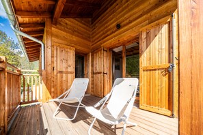 A wooden deck with two white lounge chairs, a wooden door, and a metal pipe.