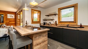 A modern kitchen with a wooden island, bar stools, and a large window. - Chalet Nanouk - exposé plein sud (La Salle-les-Alpes)