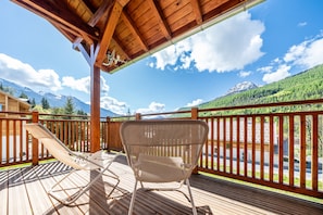 Una terraza de madera con una silla de salón y una silla de mimbre, con vistas a un paisaje montañoso.
