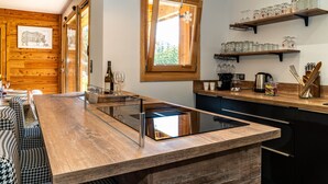 A modern kitchen with wooden cabinetry, a built-in island, and a window with a snowflake decoration. - Chalet Nanouk - exposé plein sud (La Salle-les-Alpes)