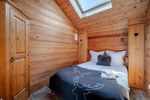 Ein Holzhütten-Zimmer mit einem Bett, einem Oberlicht und einer Tür mit Herz-förmigem Ausschnitt.