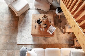 Ein Holztisch mit einer Flasche, Gläsern und einer Zeitschrift in einem gemütlichen Raum mit Fliesenboden und einer Holztreppe.