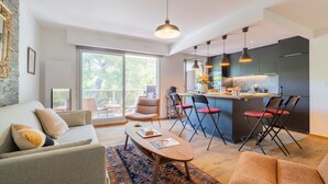 Ein modernes Wohnzimmer mit einer Couch, einem Couchtisch und Sesseln. Es gibt eine Küchenzeile mit einer Bar und Sitzgelegenheiten.