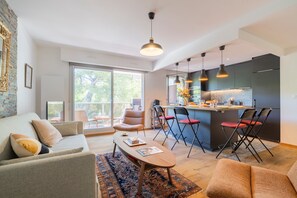 A modern living room with a sofa, coffee table, and chairs. There is a kitchen area with a bar and seating. - Match Point - À moins d'1 km des plages (Marseille)