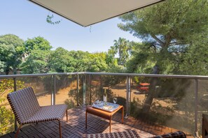 A balcony with a wicker chair, a small table with a bottle and glasses, and a view of trees and a building. - Match Point - À moins d'1 km des plages (Marseille)