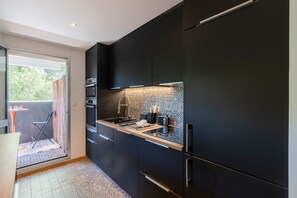 A modern kitchen with dark cabinetry, a tiled backsplash, and a small dining area with a table and chairs. - Match Point - À moins d'1 km des plages (Marseille)