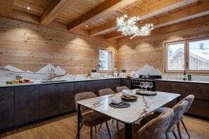 A modern kitchen with wooden walls, a marble countertop, and a dining area with chairs. - Mas Monts  - somptueuse propriété face au massif des Écrins (Le Monêtier-les-Bains)