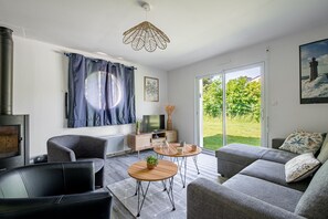 A modern living room with a fireplace, sofa, coffee table, and a view of the outdoors. - Ty Kerdreven - Maison familiale avec grand jardin (Crac'h)