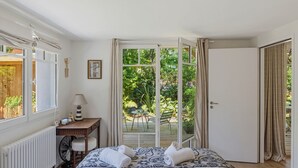 Een slaapkamer met een bed, een bureau, een stoel en uitzicht op een tuin door een glazen deur.