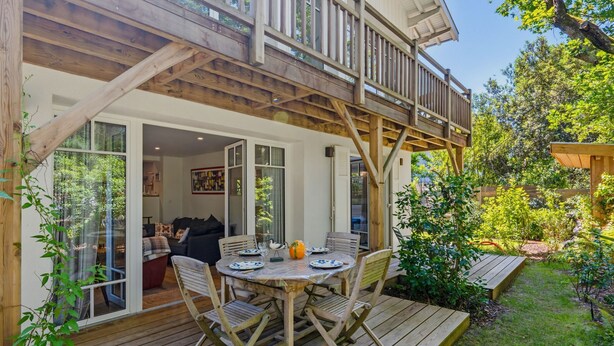 Een houten terras met een tafel en stoelen, een overdekte patio en een uitzicht op het interieur.
