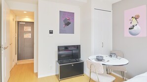 A modern hotel room with a flat-screen TV, a dining table with chairs, and artwork on the walls.