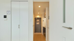 Un pasillo estrecho con suelo de madera, paredes blancas y una puerta que da a una zona de cocina.