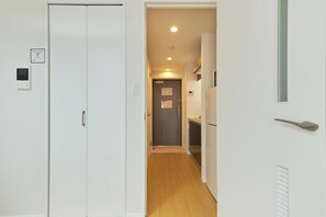 Un pasillo estrecho con suelo de madera, paredes blancas y una puerta que da a una zona de cocina.