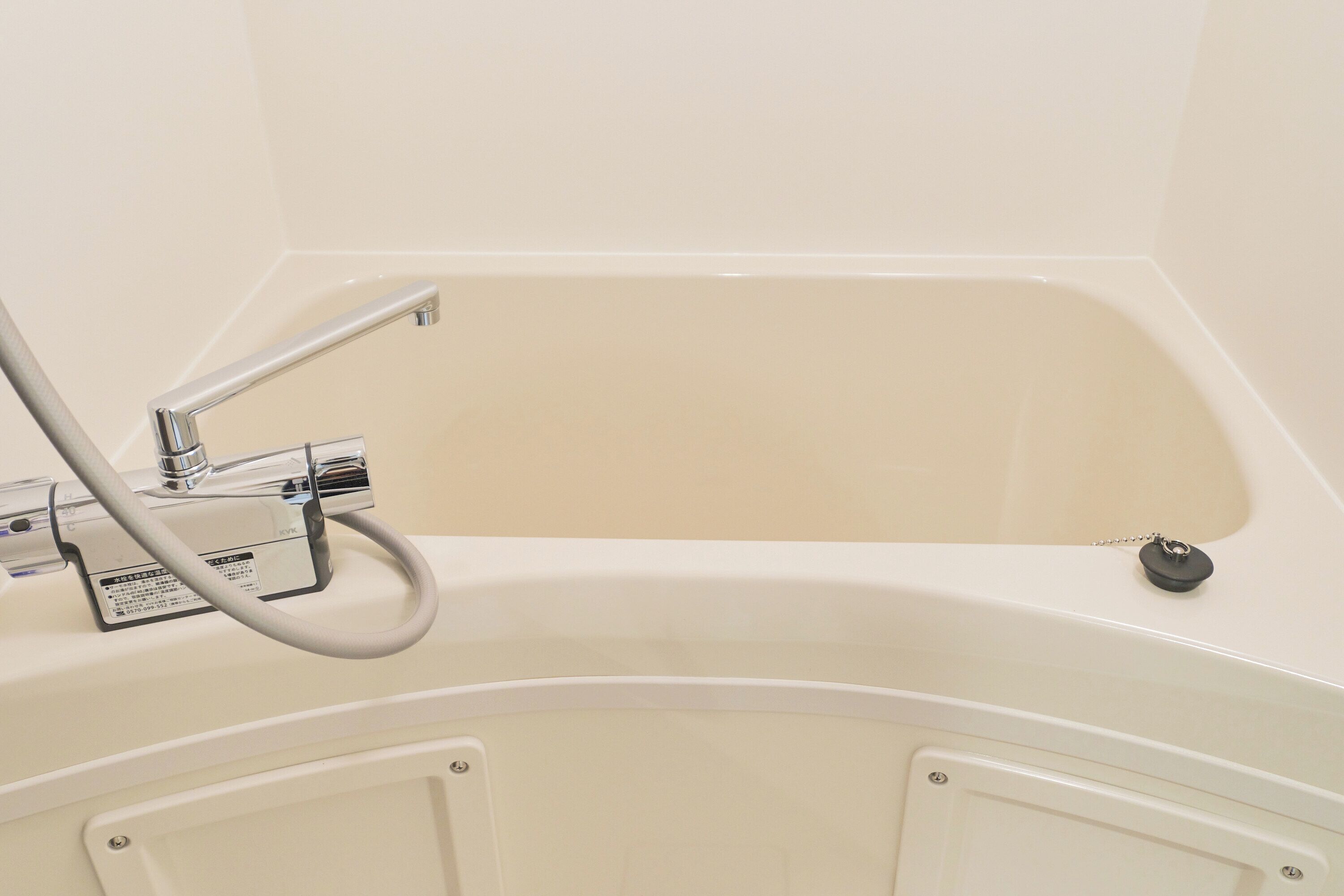 A white bathtub with a handheld showerhead and a control panel.