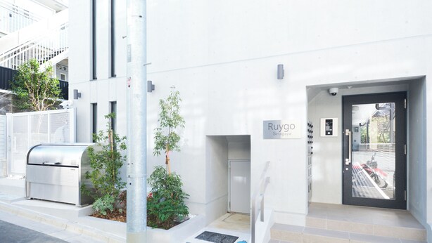 Una entrada de edificio moderna con un letrero que dice 'Ruygo', un buzón de metal y un pequeño jardín.