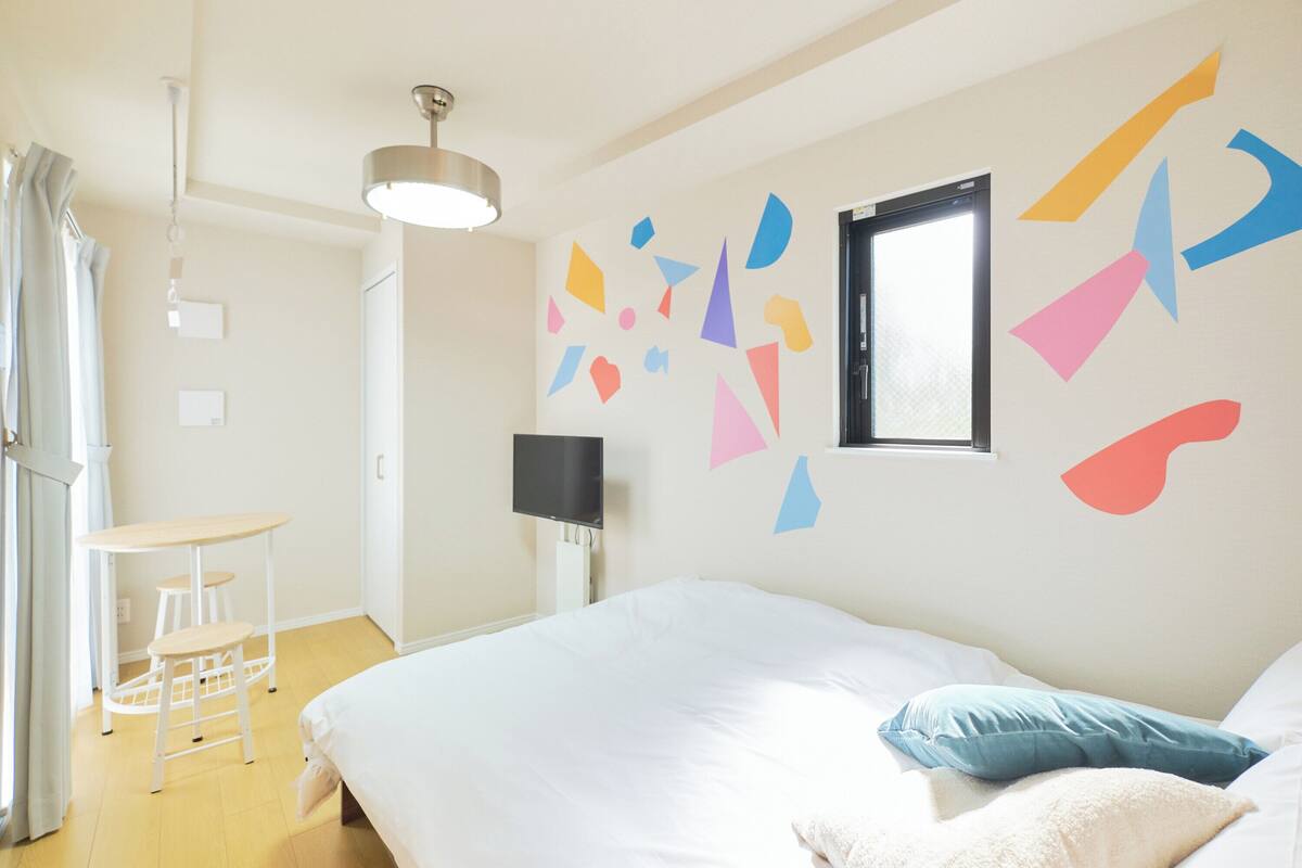 Quarto com cama, escrivaninha, cadeira, televisão e janela.