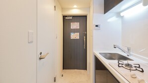 A narrow hallway leading to a door with a handle and a lock, a small sink with a faucet, and a gas stove with knobs.