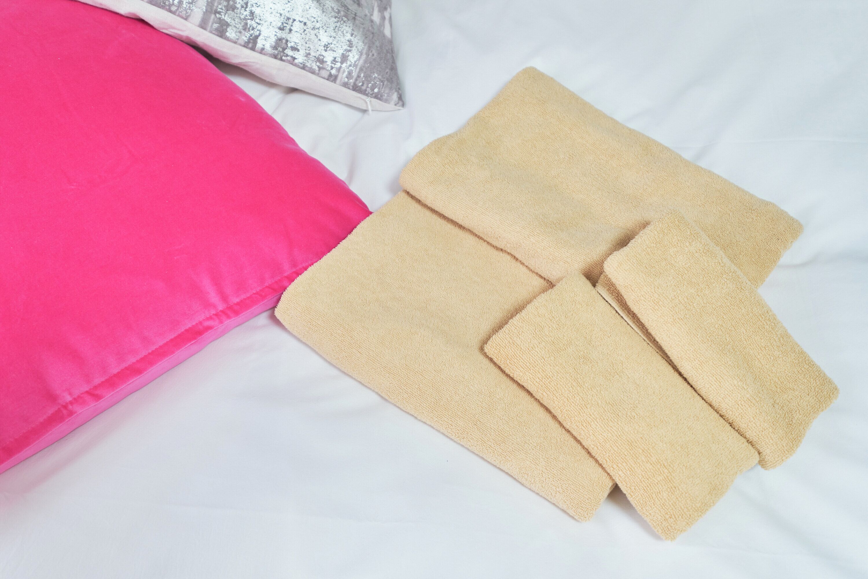 A bed with a white sheet, a pink pillow, and two beige towels.
