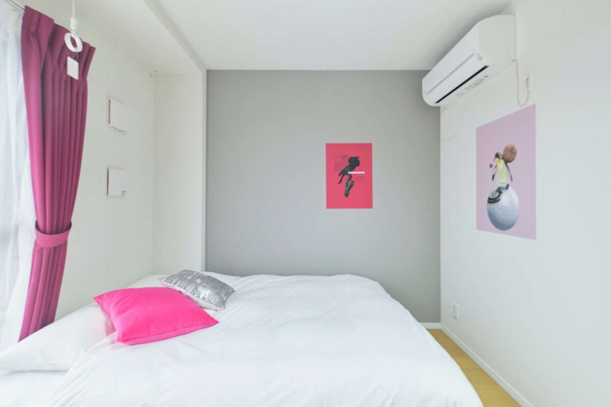 Un dormitorio con una cama, aire acondicionado instalado en la pared y dos obras de arte decorando las paredes.