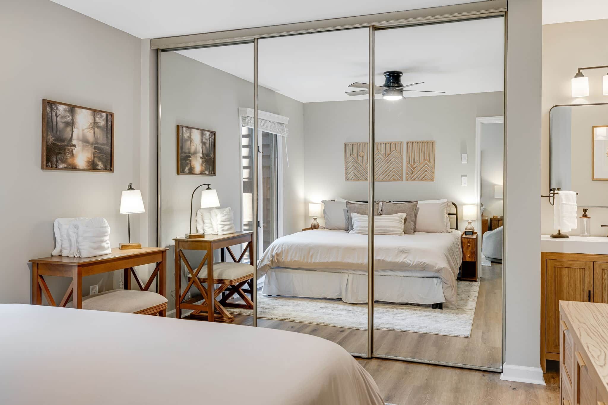 A bedroom with a large bed, a desk, a chair, a mirror, and a ceiling fan.
