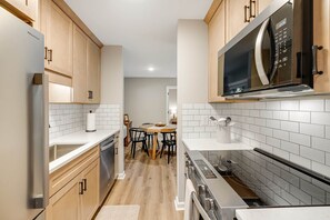Cozinha moderna com armários de madeira, micro-ondas de aço inoxidável e painel de azulejos branco.