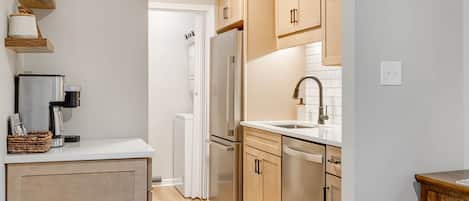 Una cocina compacta con armarios de madera, un refrigerador de acero inoxidable, una cafetera y un lavamanos.